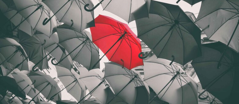 red umbrella amongst black and white umbrellas