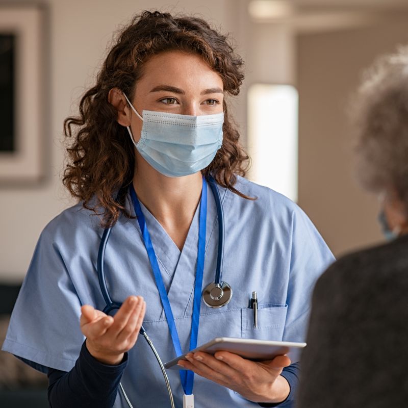 nurse wearing clinical mask speaking with a woman